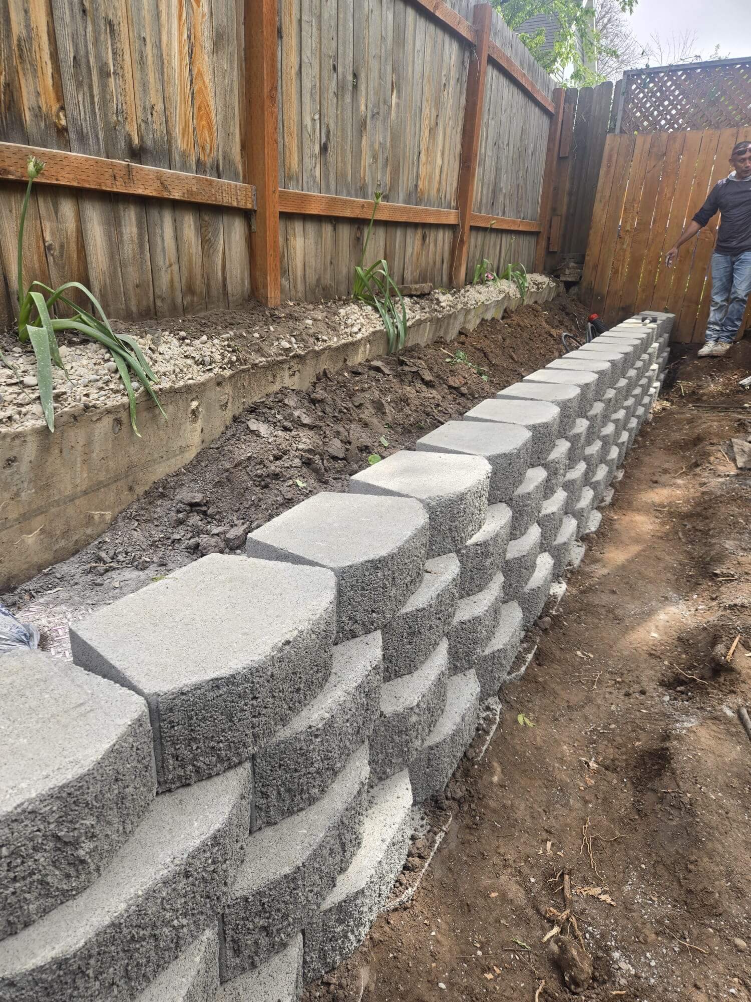 Segmental block retaining wall being built along a wood fence line