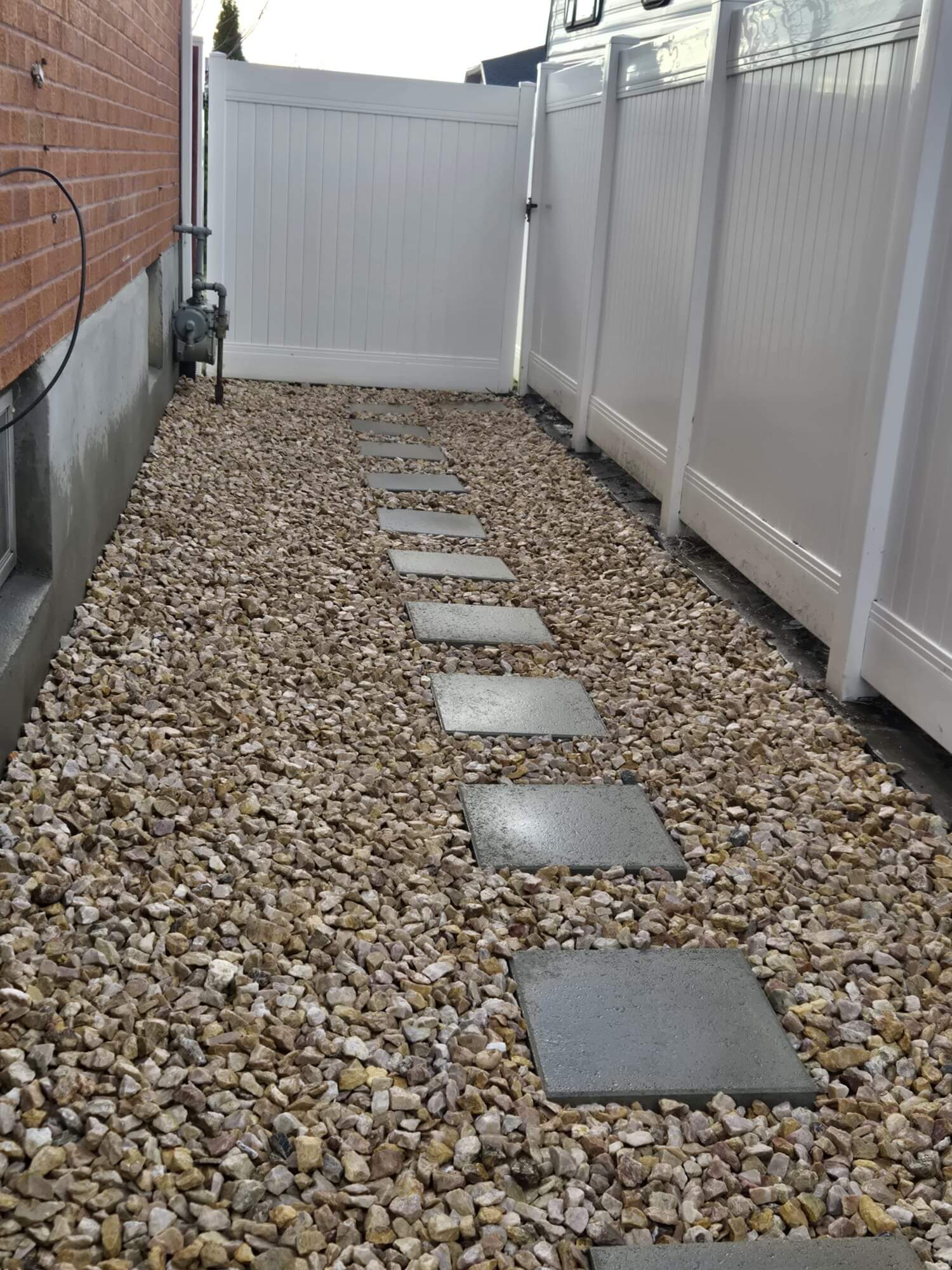 Concrete stepping stones set in decorative gravel along a vinyl fence